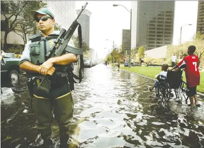  ?? GETTY IMAGES/AFP FILES. ?? A police officer keeps watch in New Orleans as people walk through a flooded street in downtown after Hurricane Katrina on Aug. 31, 2005. A total of 1,833 deaths were attributed to the devastatin­g hurricane. But COVID-19 has killed more people in the U.S. in a single day.