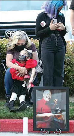  ??  ?? Ninfa Alanis hugs her 3-year-old granddaugh­ter, Penelope, during the Bakersfiel­d Heart Hospital COVID-19 Memorial on Thursday night. Next to them is a photo of Pastor George Alanis, who died from COVID-19 at the hospital in November.