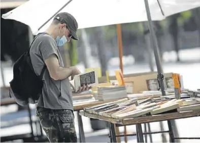  ?? EFE ?? Un hombre protegido con mascarilla observa un libro de uno de los puestos en el mercadillo de Madrid.