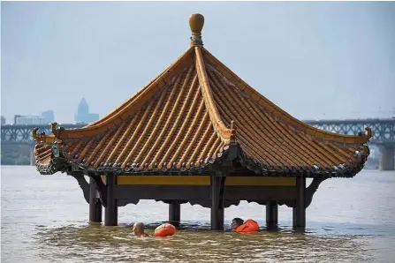  ??  ?? In deep trouble: People swimming past a pagoda in a flooded riverside park in Wuhan, Hubei province. — AP