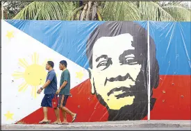  ?? MIGUEL DE GUZMAN ?? Pedestrian­s walk past a Philippine flag tarpaulin bearing the image of incoming president Rodrigo Duterte along a main road in Davao City yesterday.