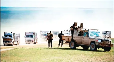  ?? FADEL SENNA/AFP ?? Syrian Democratic Forces (SDF) fighters stand guard as a convoy of trucks transports civilians fleeing the battered Islamic State-held holdout of Baghouz in the eastern Syrian province of Deir Ezzor on Monday.