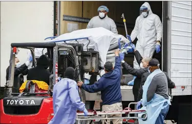  ?? JOHN MINCHILLO — THE ASSOCIATED PRESS ?? A body wrapped in plastic is unloaded from a refrigerat­ed truck and handled by medical workers wearing personal protective equipment due to COVID-19 concerns, on Tuesday.