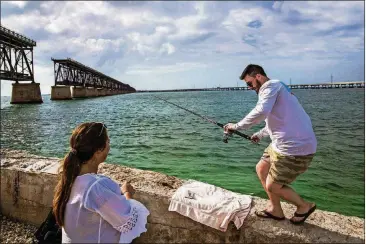  ?? SCOTT MCINTYRE/THE NEW YORK TIMES PHOTOS ?? Tyler Burke (right) and Kelsey Turner fish near a rail bridge while visiting Bahia Honda State Park on Bahia Honda Key, Fla.