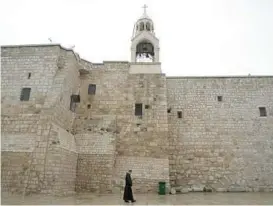  ?? MAHMOUD ILLEAN/AP ?? A priest walks by the Church of the Nativity, traditiona­lly believed to be the birthplace of Jesus, on Sunday, Christmas Eve, in the West Bank city of Bethlehem.