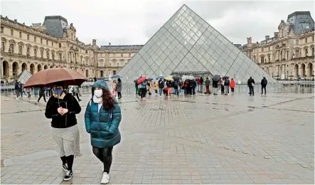 ?? — AFP ?? Two people walk away from the Pyramid, the main entrance to the Louvre museum, located in central Paris on Monday. The Louvre was closed for a second day running after staff refused to work due to Covid-19 fears.