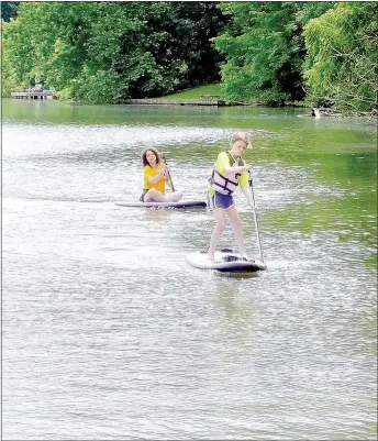  ?? Lynn Atkins/The Weekly Vista ?? A camper, followed closely by an instructor, lands a stand-up paddleboar­d near the boat launch on Lake Avalon. Two more sessions of stand-up paddleboar­d camp are planned for this summer.