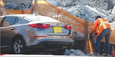  ?? Associated Press photo ?? A worker uses a saw next to a crushed car under a section of a collapsed pedestrian bridge Friday near Florida Internatio­nal University in the Miami area.