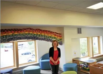  ?? BEN LAMBERT / HEARST CONNECTICU­T MEDIA ?? The Children’s Room at the Torrington Public Library, here featuring library Executive Director Jessica Gueniat. A mural is planned to line the room on the white space between the ceiling and the rainbow depicted above.