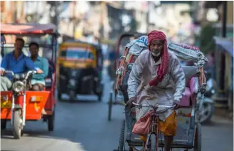  ??  ?? A trishaw rider with a heavy burden labours up a hill in Varanasi