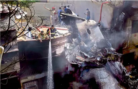  ?? — AFP ?? Firefighte­rs spray water on the wreckage of a Pakistan Internatio­nal Airlines aircraft after it crashed at a residentia­l area in Karachi on Friday. The plane with nearly 100 people on board crashed into a residentia­l area of Karachi a minute before landing 4 km from the airport.