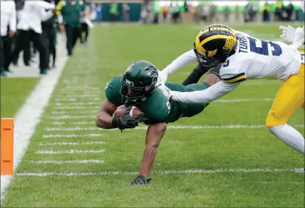  ?? AL GOLDIS / ASSOCIATED PRESS ?? Michigan State’s Kenneth Walker III, left, dives over the goal line for one of his five touchdowns Oct. 30 against Michigan in East Lansing, Mich. The Spartans, who remained undefeated following a 37-33 win against their in-state rival, were ranked third in the first College Football Playoff rankings released Tuesday.