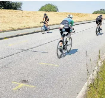  ?? FOTO: WENDT/DPA ?? Triathlete­n fahren auf dem Rad an der Unglücksst­elle auf dem Gaueter Hauptdeich in der Nähe von Hamburg vorbei, bei dem am Sonntag ein Motorradfa­hrer ums Leben kam und ein Wettkämpfe­r schwer verletzt wurde.