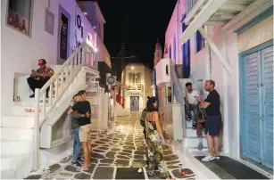  ?? (Louiza Vradi/Reuters) ?? TOURISTS LINGER in front of closed shops and restaurant­s in Mykonos town yesterday as Greece banned music in restaurant­s and bars and imposed a nighttime curfew on the island.