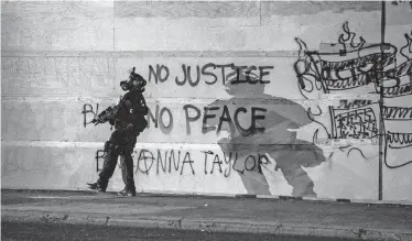  ??  ?? On Aug. 24, a police officer walked past a wall of graffiti calling for racial justice outside the Portland Police Associatio­n building in Portland, Ore. Over the decades, the Republican Party has participat­ed less in the conversati­on on solutions to urban problems.