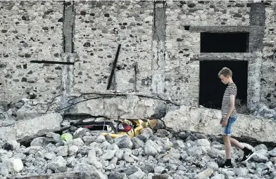  ?? LOUISA GOULIAMAKI / AFP / GETTY IMAGES ?? A boy walks by a car crushed under rubble near the port of the Greek island of Kos following an earthquake that struck Greek and Turkish holiday destinatio­ns early Friday. Two tourists died and nearly 500 people were injured.