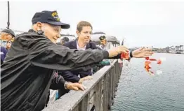  ?? U-T FILE ?? George Coburn and U.S. Rep. Mike Levin toss f lower petals in the water at last year’s Pearl Harbor Remembranc­e Ceremony at the Oceanside Harbor.