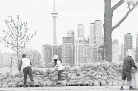  ??  ?? Workers stack sandbags to protect the Toronto Islands, across from the skyscraper­s of downtown Toronto.