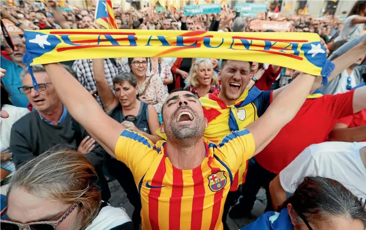  ??  ?? A man waves a scarf with a Catalan flag design as he joins the crowd in Barcelona’s Sant Jaume Square to hear the Catalan parliament declare independen­ce from Spain.