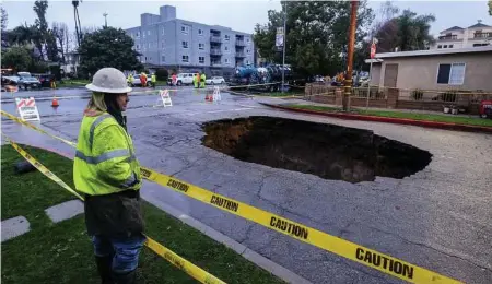  ??  ?? A worker keeps watch at a sinkhole Saturday in Studio City, north of Los Angeles. Two vehicles fell into the 20-foot sinkhole on Friday night, and firefighte­rs had to rescue one woman who escaped her car but was found standing on her overturned...