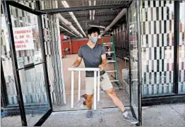  ?? ANTONIO PEREZ/CHICAGO TRIBUNE ?? Owner Edward Kim props open the front door last week as staff prepares for the reopening of City Fashions in the Lake Meadows Shopping Center in Bronzevill­e.