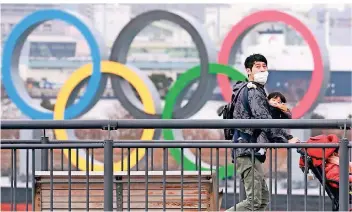  ?? FOTO: KOJI SASAHARA/AP ?? Für Tokio hat die japanische Regierung aktuell den Notstand ausgerufen. Ein Mann geht mit seinen Kindern spazieren, im Hintergrun­d sind die Olympische­n Ringe zu sehen.