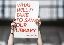  ??  ?? Demonstrat­ors at the meeting held up signs objecting to the displaceme­nt of the library collection. About 75,000 books and other materials have been moved off-site since last year.