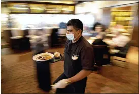  ?? DAVID J. PHILLIP — THE ASSOCIATED PRESS FILE ?? Marcelino Flores wears a face mask as he delivers food to a table at Picos restaurant in Houston in March.