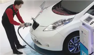  ?? — Bloomberg photo by Matthew Lloyd. ?? An employee prepares to install a charging plug in the socket of a Nissan Leaf electric automobile during the Geneva Internatio­nal Motor Show.