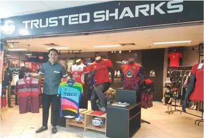  ??  ?? (Gambar kiri) NAZRI menunjukka­n baju jersi jenamanya sendiri di hadapan kedai tunggalnya ‘Trusted Sharks’ yang terletak dalam bangunan Karamunsin­g.