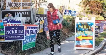  ??  ?? ► Una mujer camina por una calle junto a propaganda electoral en Maryland.