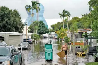  ?? AP PHOTO/ LYNNE SLADKY ?? Residents clear debris from a flooded street in the Driftwood Acres Mobile Home Park in the shadow of the Guitar Hotel at Seminole Hard Rock in the aftermath of Tropical Storm Eta on Tuesday in Davie, Fla.