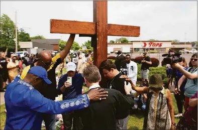  ?? Joshua Bessex / Associated Press ?? A group prays at the site of a memorial for the victims of the Buffalo supermarke­t shooting outside the Tops Friendly Market on Saturday in Buffalo, N.Y. Tops was encouragin­g people to join its stores in a moment of silence to honor the shooting victims Saturday at 2:30 p.m., the approximat­e time of the attack a week earlier.