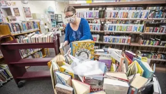  ?? Andrew Rush/Post-Gazette ?? Amy Ohliger, assistant children’s librarian at Dormont Library, picks up books that have been through a four-day quarantine before returning them to shelves Thursday.