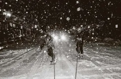  ?? Stephen Maturen / Getty Images ?? Snowboarde­rs ride behind an SUV as snow continues to fall Wednesday in Minneapoli­s. Temperatur­es in the mid-40s were giving way to high winds and heavy snowfall as forecaster­s warned of blizzards across the region.