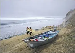  ?? Nelvin C. Cepeda San Diego Union-Tribune ?? SURFERS WALK by a suspected smuggling boat Sunday on Black’s Beach in San Diego County. “Several life jackets and fuel barrels were also found,” officials said.