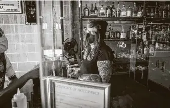  ??  ?? Owner Lindsay Rae Burleson stands behind plexiglass that surrounds the bar at Two Headed Dog in Midtown. She also works at a distillery and sells mixers at farmers markets.