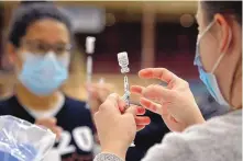  ?? JIM THOMPSON/JOURNAL ?? Lily Ouellett, right, and Angela Owens, left, tap syringes filled with the COVID-19 vaccine to remove any air bubbles before the shots are administer­ed.