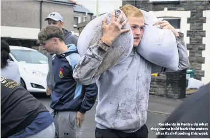  ??  ?? > Residents in Pentre do what they can to hold back the waters after flash-flooding this week