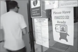  ?? The Associated Press ?? ID REQUIRED: In this May 5, 2014, file photo, a voter walks past a “Please Have Photo ID Ready” sign as he enters an early-voting polling place in downtown Little Rock. Arkansas’ revived law requiring voters to show photo identifica­tion before casting...