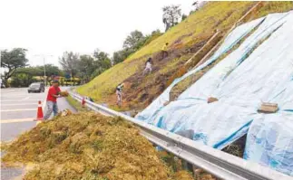  ??  ?? DBKL workers placing a canvas on the fissures in the slope at Jalan 11/55C, Puncak Setiawangs­a, Bukit