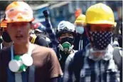  ?? AP ?? Anti-coup protesters wearing helmets and masks take positions as police gather in Yangon, Myanmar on Friday. Myanmar’s military, fresh off a coup, has killed scores of unarmed protesters.