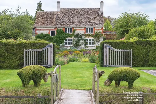  ??  ?? Topiary sheep graze beyond the yew hedging and mixed perennial beds.