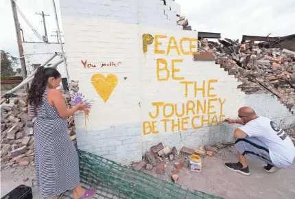  ??  ?? Eric Prostco paints a message on the remains of the Danish Brotherhoo­d Lodge. With him is his daughter, Payton, 10.