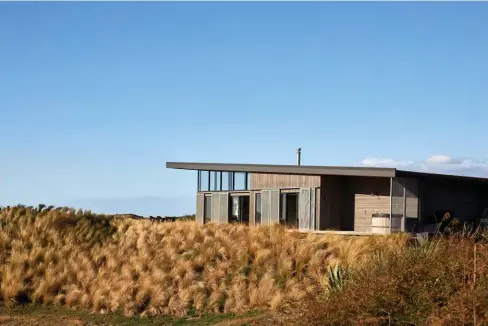  ??  ?? BELOW Materials inside and out take their cue from the environmen­t. The silvery stained-cedar battens reference the driftwood piled up on the beach, the organic nature of the concrete slab underfoot is similar to the sand, and the plywood on the ceiling is the same shade as the surroundin­g tussocks. Even the cedar hot tub blends in.