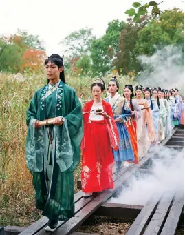  ?? ?? Students from Hangzhou Wanxiang Polytechni­c in traditiona­l outfits walk the wooden runway at Xixi Wetland.