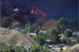  ?? Dan Watson/The Signal ?? Flames approach a community near Grand Canyon Road in Canyon Country as a water-dropping helicopter passes over last week. Investigat­ors continue to look for the cause of the Tick Fire, which endangered more than 10,000 SCV homes.