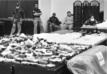  ??  ?? An unidentifi­ed Taiwanese (centre) being guarded by armed Indonesian National Narcotics Agency’s officers next to some methamphet­amines and Nimetazepa­m pills during a press conference in Jakarta yesterday.The BNN conducted a raid to a warehouse and...