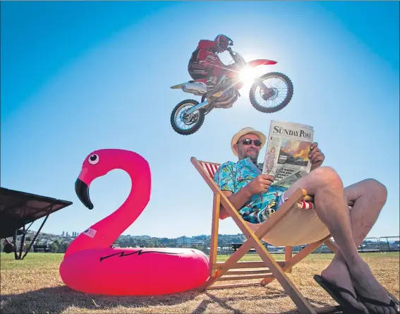  ?? Picture Andrew Cawley ?? Stuntman Mike Abernethy enjoys his favourite Sunday read as a motorcycli­st soars above him at Greenock’s Battery Park