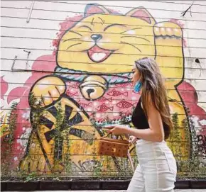  ?? AFP PIC ?? A woman walking past a mural of a Maneki-neko, or beckoning cat, in an alley in Hanoi yesterday.